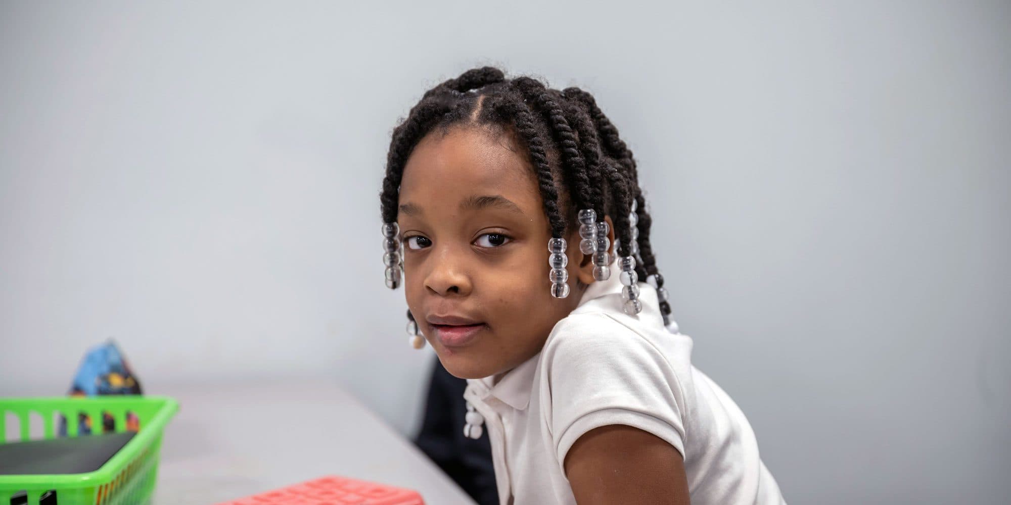 Young student with beaded braids sitting at a classroom table.