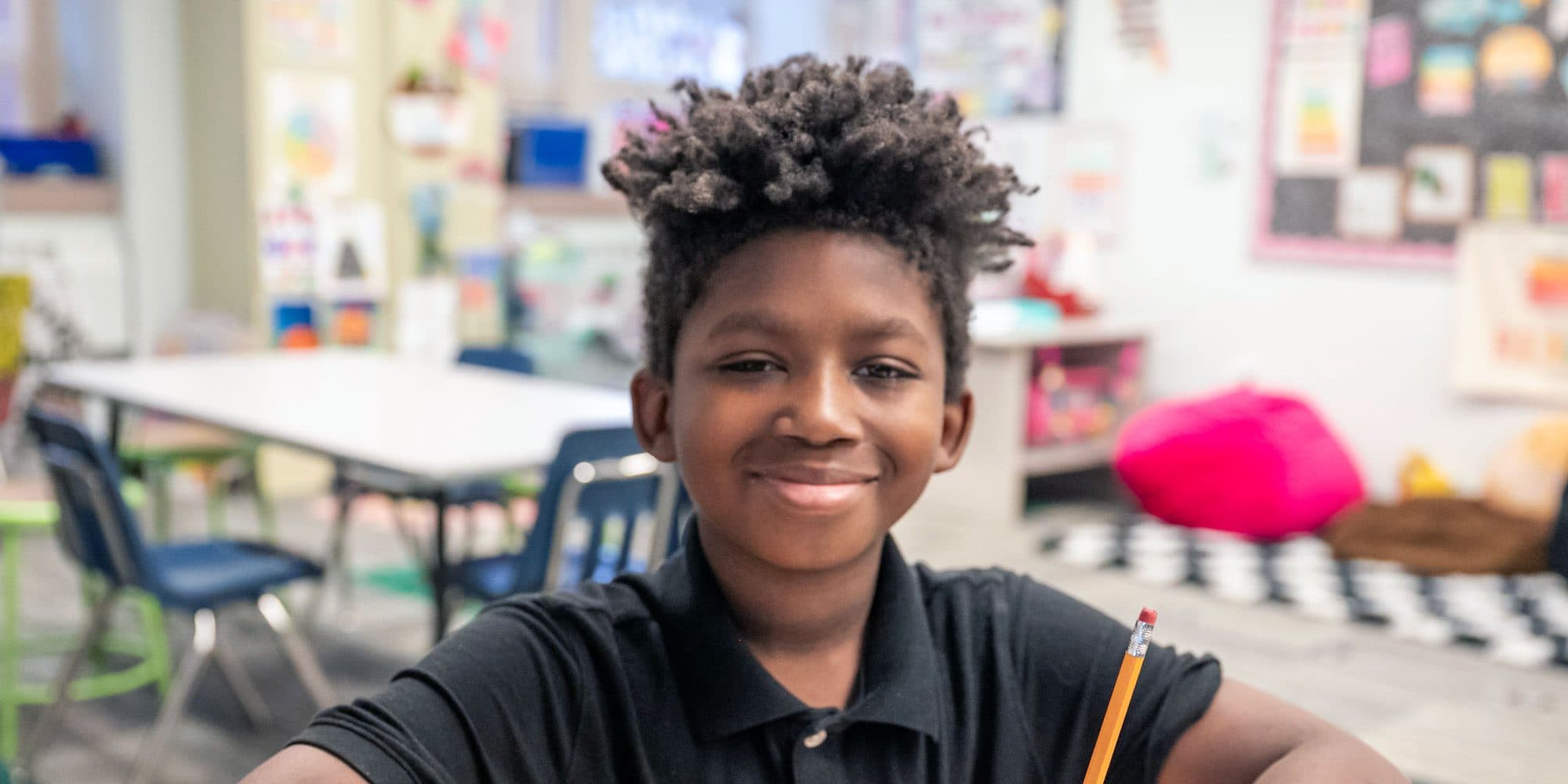 Smiling student holding a pencil in a bright classroom.