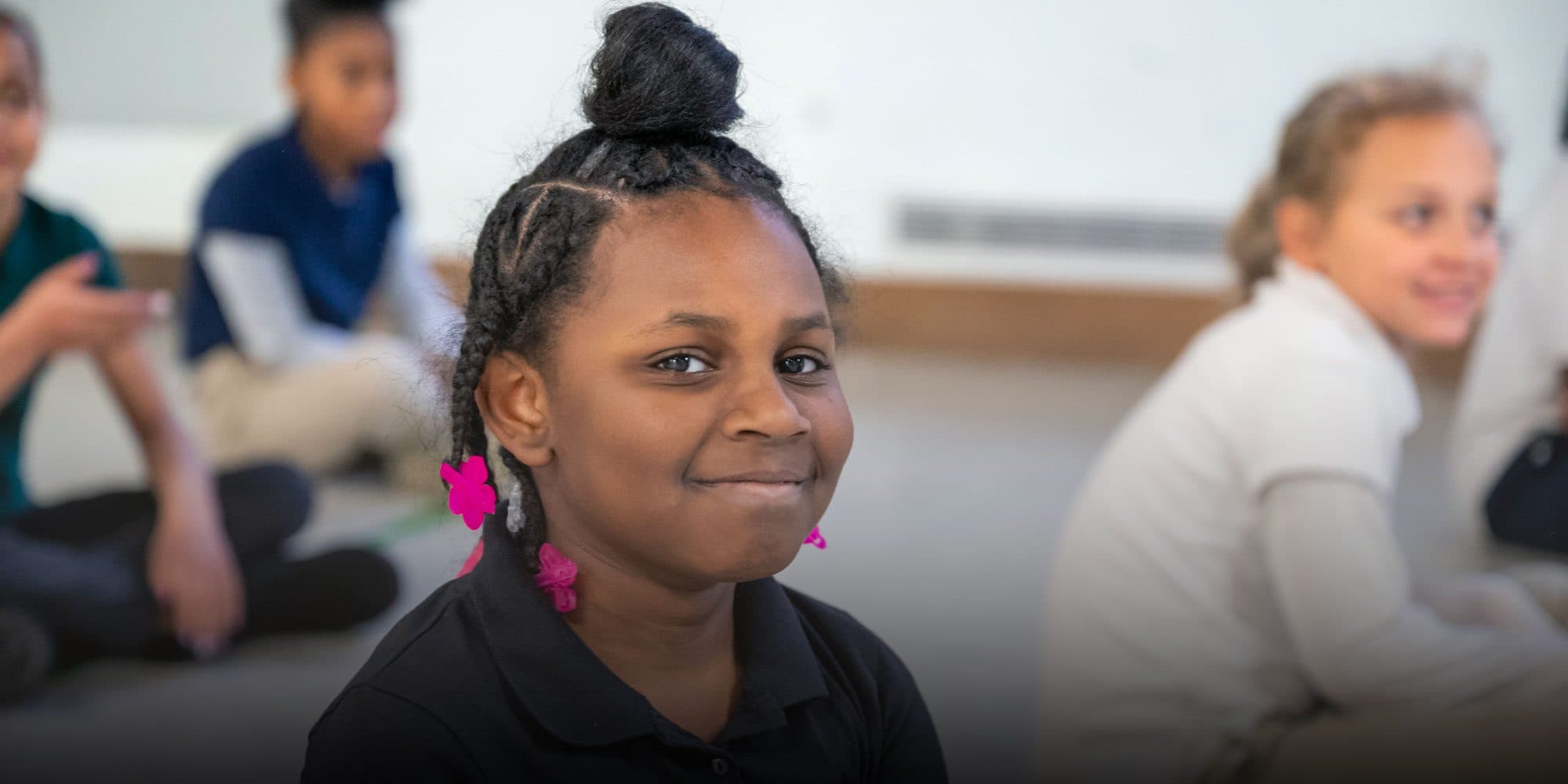 Smiling student with pink hair accessories sitting with classmates.