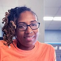 Smiling adult with dreadlocks and glasses.