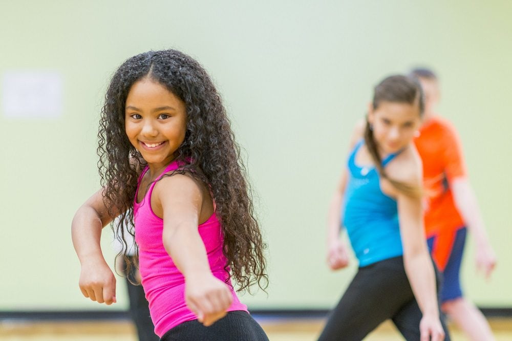 Smiling child in pink tank top dancing with a group.