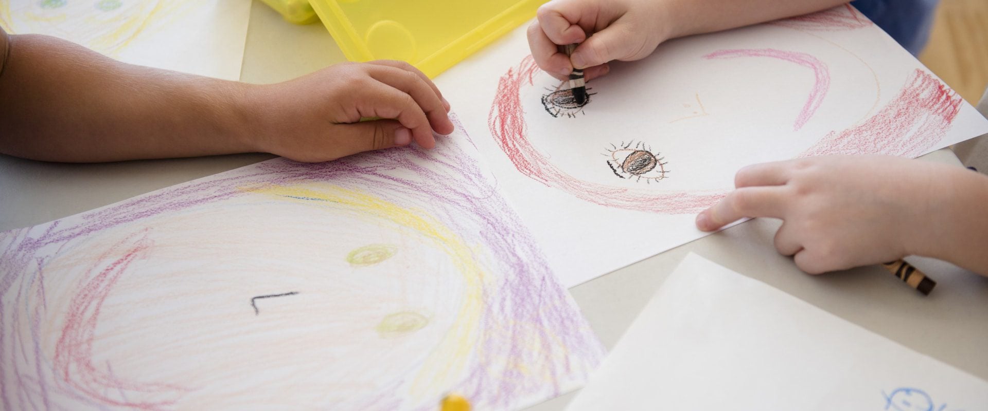Children's hands coloring drawings of faces with crayons.